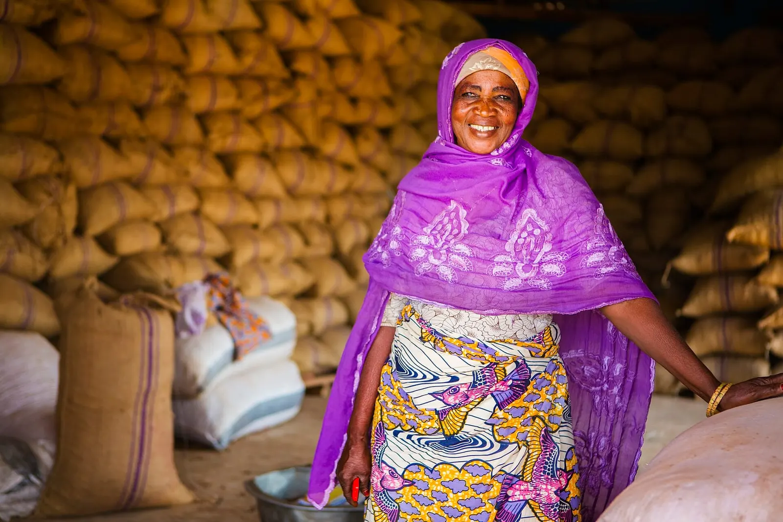A shea business owner smiling in a warehouse stacked with sacks of shea